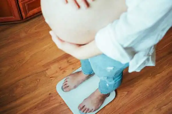 Image of woman weighing herself and experiencing weight gain through pregnancy Shropshire